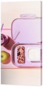 The concept of healthy school meals. Food composition with lunch box with yogurt, cereal bar, apple and oatmeal berries cocktail on a pink background with window light. Flat lay, horizontal banner