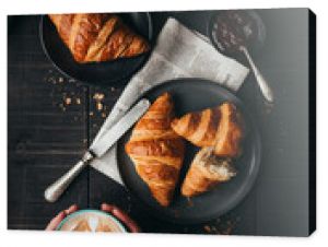 Hands holding latte beside croissants on black table from above.