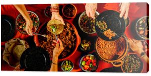 Overhead shot of a dinner table with Mexican food and hands. Tacos, beans, carnitas, habanero, salsa