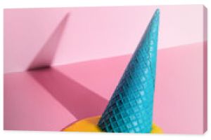 An overturned waffle cone with melted ice cream on a pink background.