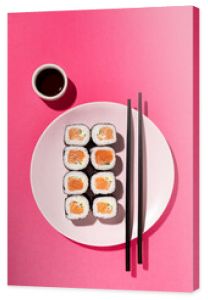 Japanese Sushi roll with salmon, cucumber and soy sauce with chopsticks in the plate on pink background with hard shadow. Concept food photography. Top view and copy space