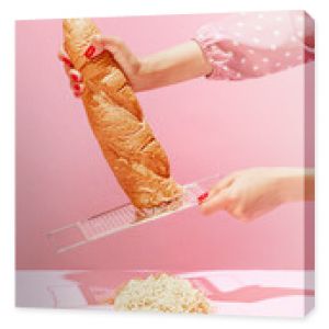 Female hands grating bread, baguette to make breadcrumb for meat isolated over pink background