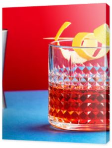 Sazerac, alcoholic cocktail drink with cognac, bourbon, absinthe, bitters, sugar and lemon zest. Dazzling red blue background with hard light and shadows pattern