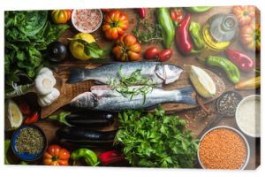 Raw uncooked seabass fish with vegetables, grains, herbs and spices on chopping board over rustic wooden background