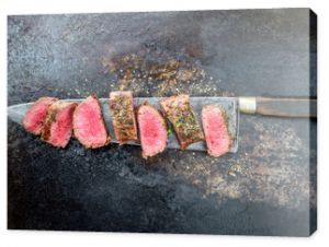 Traditional barbecue aged venison backstrap roast sliced with herbs as top view on a large knife with rustic background with copy space