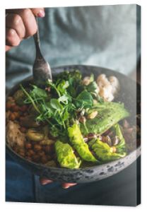 Healthy dinner or lunch. Woman in t-shirt and jeans eating vegan superbowl or Buddha bowl with hummus, vegetable, salad, beans, couscous and avocado