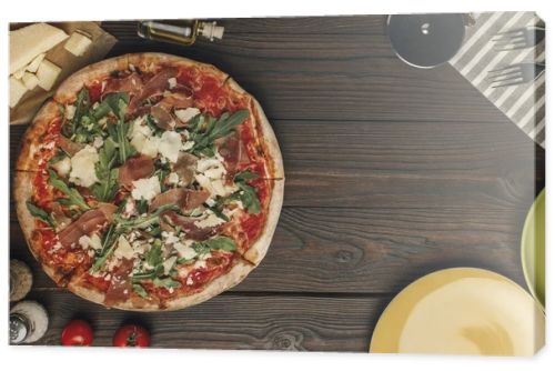 flat lay with arranged italian pizza, cutlery and various ingredients on wooden surface