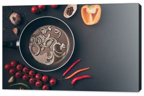 top view of frying pan with onion and oil among vegetables on gray table 