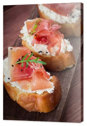 Baguette with cottage cheese, arugula and ham, sandwich on a board, selective focus. Wooden rustic background. Top view