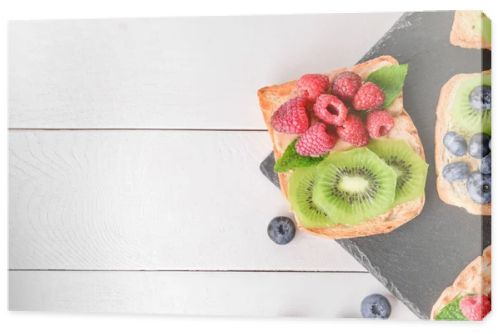 Slate plate with tasty sandwiches, kiwi and berries on white table