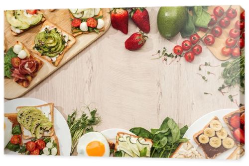 top view of toasts with vegetables, fruits and prosciutto with greenery and ingredients on wooden table