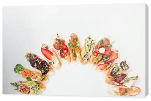 top view of delicious traditional italian bruschetta with prosciutto, salmon, fruits, vegetables and herbs on white