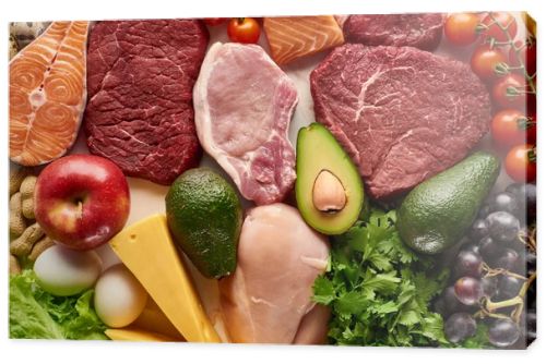 Top view of assorted raw meat, poultry, fish, eggs, vegetables, fruits, nuts, greenery and cheese 