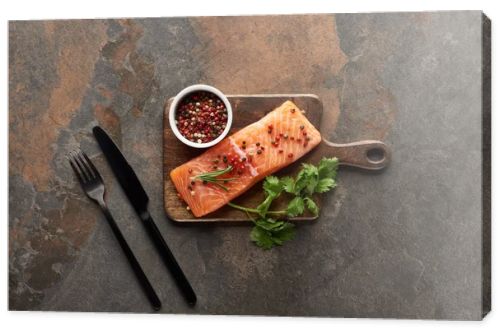 top view of raw fresh salmon with peppercorns, parsley on wooden cutting board near cutlery