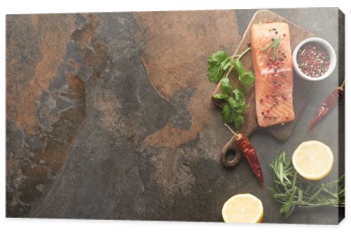 top view of raw fresh salmon with greenery, chili peppers and lemon on wooden cutting board