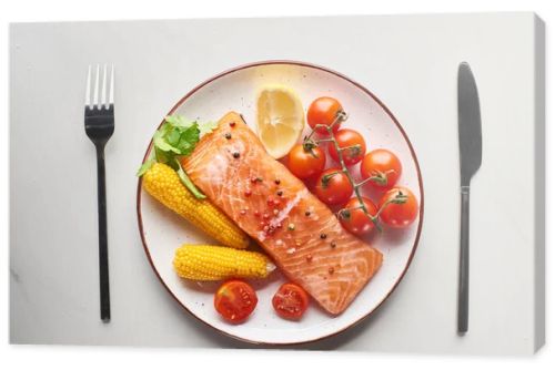 top view of raw salmon steak served with corn and tomatoes on plate near cutlery on marble table