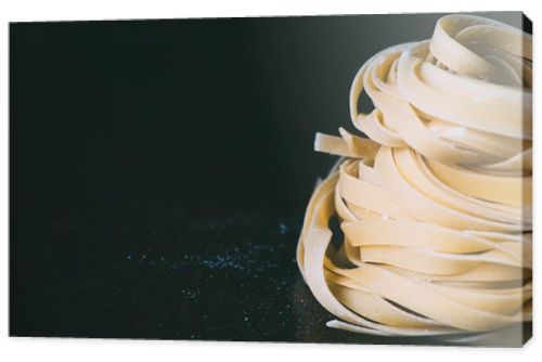 closeup view of raw tagliatelle pasta covered by flour on black background 