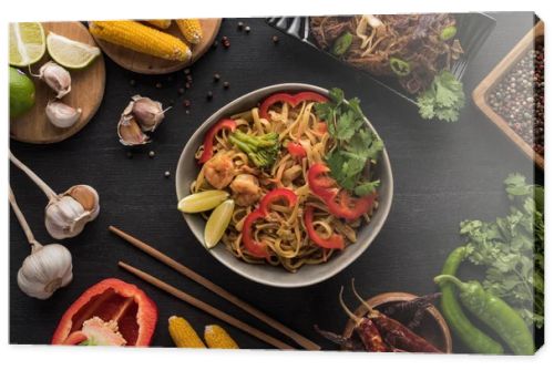 top view of tasty spicy seafood thai noodles near chopsticks and fresh ingredients on wooden grey surface