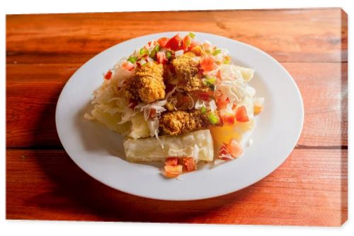 Traditional chicharron dish with cassava and tomato salad. Latin food chicharron con yuca served on wooden table. Nicaraguan dish chicharron with cassava on the table.