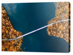 Aerial view of bridge road with red car over blue water lake or sea with island and autumn color woods in Finland.